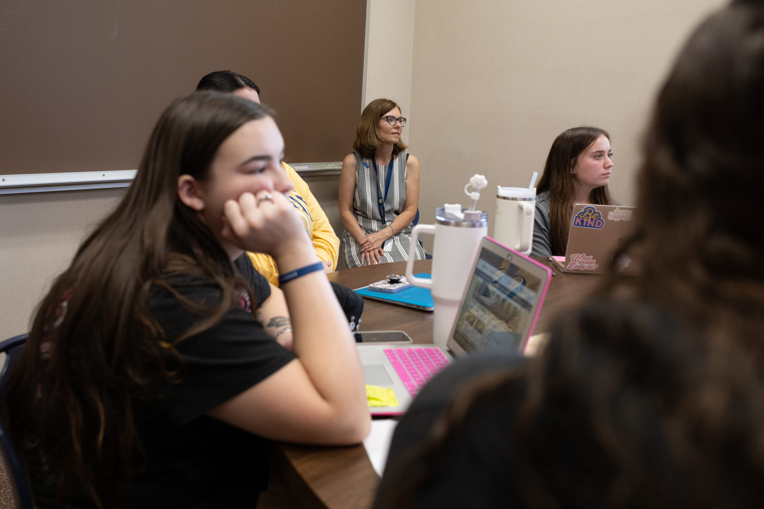 Students sit around a table with Dr. Harder listening to a peer speak